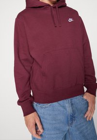 Sudadera Nike color marrón con un bolsillo tipo canguro, capucha ajustable y un acento de logo blanco. Material suave con puños y dobladillo acanalados.