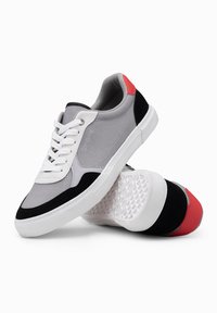 Šedé tenisky s černými a červenými akcenty, s textilním svrškem, bílými tkaničkami a texturovanou gumovou podešví.