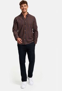 Brun og marineblå ternet skjorte med knapper og lange ærmer; kombineret med mørke bukser og hvide sneakers.