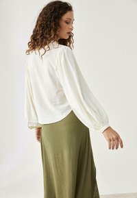 Blusa blanca de manga larga con hombros fruncidos, combinada con una falda larga verde oliva con un acabado texturizado.