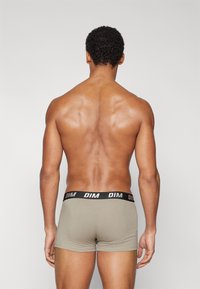Beige boxer shorts fekete DIM logo-val ellátott derékkal, szoros szabással és puha textúrával, hátulról látható, további részletek nélkül.