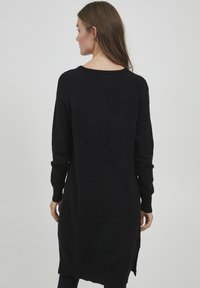 Schwarzes, langärmliges Strickkleid aus einem weichen Stoff, mit lockerem Schnitt, Seitenschlitzen und einem weiten Ausschnitt. Einfaches, minimalistisches Design.