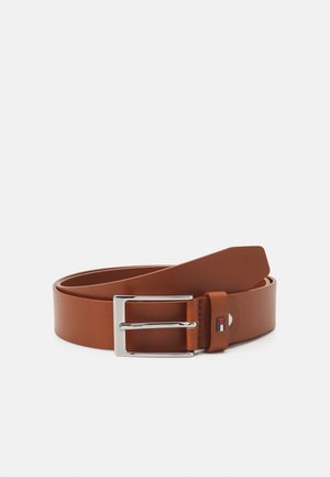 Ceinture en cuir marron avec boucle rectangulaire argentée et petit détail du logo rouge, blanc et bleu sur la boucle, enroulée sur fond blanc.