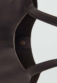 Intérieur du sac en cuir marron, présentant une texture lisse avec un revêtement en daim. Comprend une fermeture à pression métallique ronde et des poignées allongées.