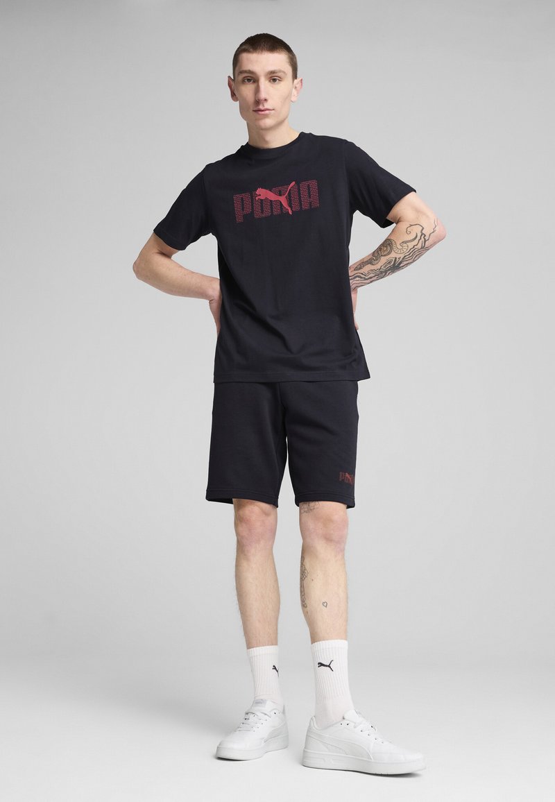 Melnas kokvilnas T-krekls ar sarkano Puma logo, kombinēts ar melniem šortiem. Modelis valkā baltas kedas un potītes zeķes ar Puma logo.