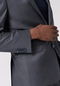 Grau maßgeschneiderte Blazer aus glattem Stoff, mit einer einzigen Brusttasche und einem vierknopfigen Detail am Ärmel in kontrastierendem Blau.