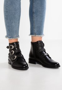 Černé kožené kotníkové boty s třemi přezkami se stříbrným kováním, s nízkým blokovým podpatkem a zipem na boku.