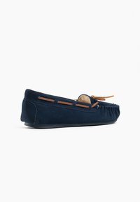 Marineblaue Wildleder-Mokassins mit flacher Gummisohle, die mit Leder-Schnürungen und einer abgerundeten Zehenpartie für ein klassisches Design ausgestattet sind.