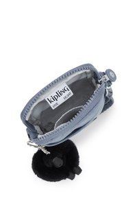 Liten blå Kipling-plånbok med öppen dragkedja, som visar det tomma inuti och varumärkesetikett, fäst svart fluffig nyckelring med plastben.