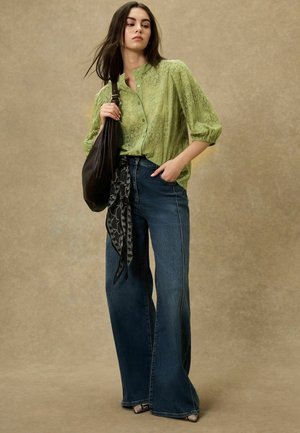 Grön spetsblus med 3/4-ärmar, kombinerad med högmidjade, vida jeans. Mörk handväska och svart mönstrad sjal kompletterar outfiten.