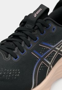 Svart atletisk sko med teksturert overdel, med blå og rosa detaljer, avrundet tå, og polstret såle for komfort.