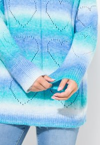 Maglione oversize lavorato a maglia in gradiente di teal e blu; presenta motivi a cuore, polsini a coste e una finitura morbida e testurizzata.