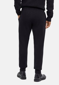 Czarne dziergane spodnie dresowe z prążkowanymi ściągaczami przy nogawkach i talii, z bocznymi kieszeniami. Noszone z czarnymi botkami za kostkę, podkreślającymi casualowy styl.