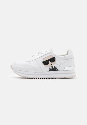 Hvid sneaker med tyk sål har et tegneserieansigt med sorte solbriller og en sort jakke på sidelåget.