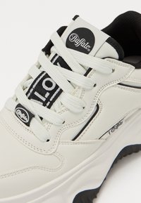 Weiße LederSneaker mit schwarzen Akzenten, ausgestattet mit runden Schnürsenkeln und einem Logoetikett auf der Zunge. Gepolsterte Sohle mit strukturiertem Griff.