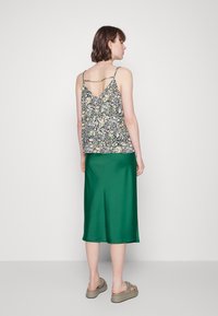 Top de alças em flores multicoloridas, costas em V, combinado com uma saia midi de cetim verde. A modelo usa sandálias cinzas.