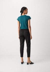 Türkiser Kurzarm-Top mit Spitze, kombiniert mit schwarzen Hose mit elastischem Bund und schlichten schwarzen Blockabsatz-Mules.