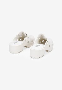 Sabots blancs épais en matériau durable avec des découpes, des semelles texturées et un design à plateforme surélevée. Logo sur la semelle intérieure.