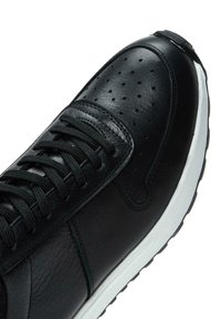 Sneaker nera in pelle con dettagli perforati, pannelli testurizzati e lacci neri piatti. Presenta una suola intermedia bianca e una suola in gomma.