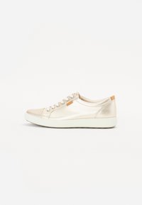 Baskets basses en cuir beige avec semelle blanche, fermeture à lacets à l'avant et petite étiquette de marque sur le côté.