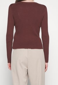 Bruine geribbelde trui met lange mouwen, voorzien van een aansluitend ontwerp en een ronde hals, gecombineerd met lichtgekleurde broek.