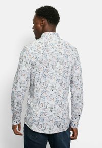 Blumenmuster-Hemd mit langen Ärmeln in Weiß mit pastellblauen, rosa und schwarzen Mustern. Verfügt über einen Button-Down-Kragen und Ein-Knopf-Manschetten.