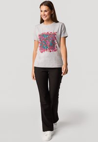 Grijze t-shirt met een kleurrijk bloemenpatroon in roze, rood en teal, gecombineerd met zwarte broek en witte sneakers.