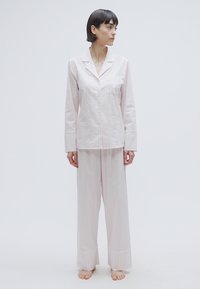 Ensemble de pyjama rose pâle comprenant une chemise à col avec boutons et un pantalon ample rayé avec larges poignets. Texture lisse, tissu en coton.