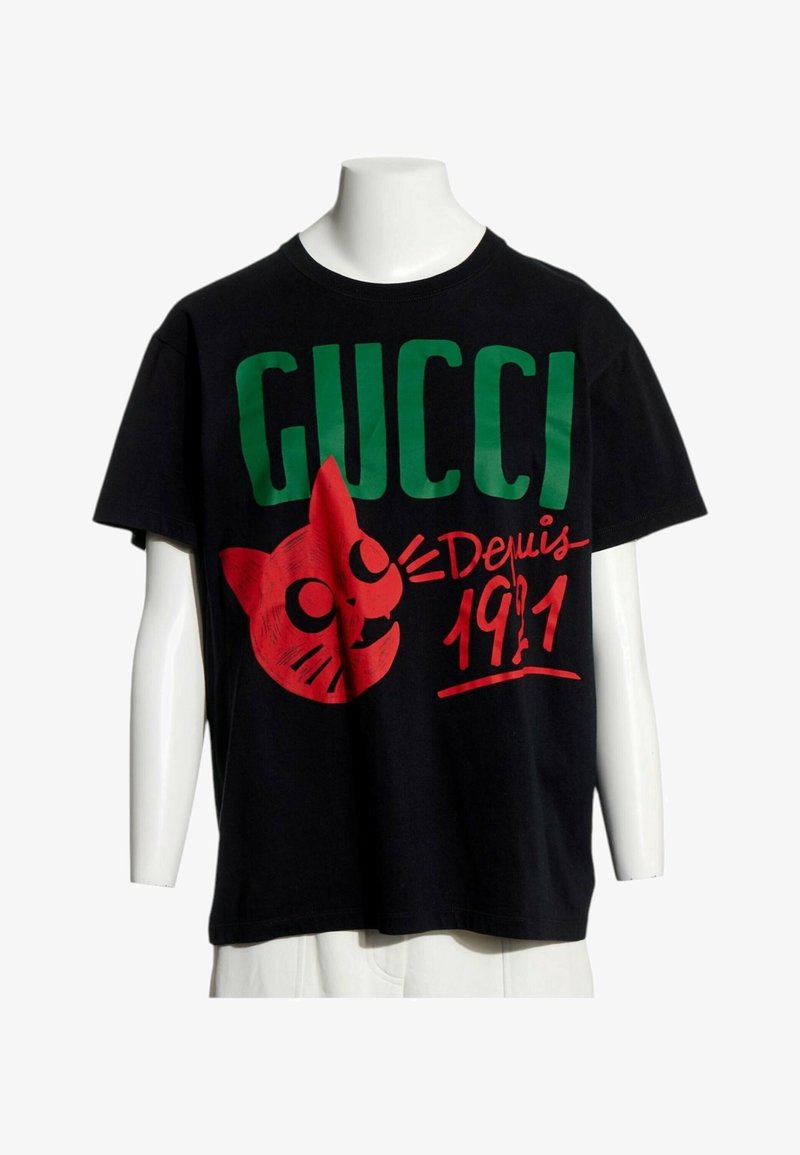 T-shirt noir à manches courtes avec un grand texte vert "GUCCI", visage de chat dessin animé rouge et écriture rouge "Depuis 1911" sur le devant.