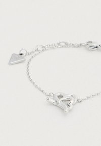 Ασημένιο βραχιόλι με σχεδίαση πλεγμένης καρδιάς, λεπτή αλυσίδα και προσαρτημένη τριγωνική ταυτότητα. Ομαλή υφή και ανακλαστική επιφάνεια.