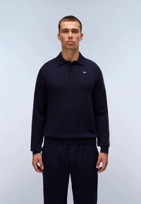 Tamsiai mėlynas megztinis iš minkštos medžiagos, turintis apykaklę, tris sagas ir mažą logotipą kairėje krūtinės pusėje.