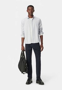 Lichtblauw overhemd met knopen, donkerblauwe broek, zwarte schoenen en een zwarte tas. Het overhemd heeft lange mouwen en een klassieke kraag.