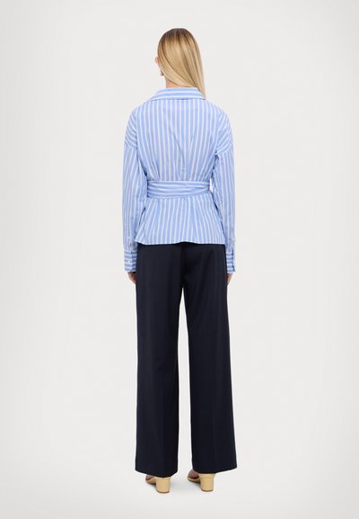Blauwe en witte gestreepte blouse met lange mouwen en een getailleerde taille, gecombineerd met zwarte wijde broek. Soepele stof met knoopdetails.