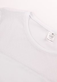 Jasnoniebieska bawełniana koszulka z panelami z przezroczystej tkaniny w kropki na górze. Okrągły dekolt o gładkim wykończeniu, metka wewnątrz.