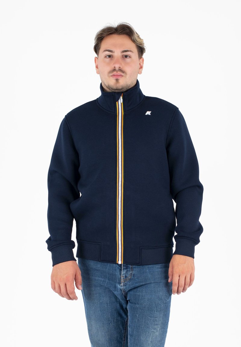 Felpa con zip navy e colletto alto, con dettagli della zip a strisce gialle e bianche e polsini a costine; il materiale sembra una miscela di cotone.