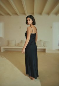 Fekete selymes maxi ruha vékony állítható pántokkal, sima textúrával és lágy sziluettel, semleges háttér előtt bemutatva.