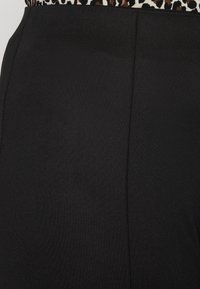 Zwarte rok met een gladde, matte afwerking en een tailleband met een luipaardprint. Verticale naadtoeslag aan de zijkant voegt structuur toe.