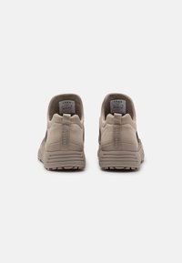 Beige Sportsneaker mit strukturiertem Obermaterial, unterstützendem Absatz und Gummisohle. Mit Ziehlasche und Markenlogo am Absatz.