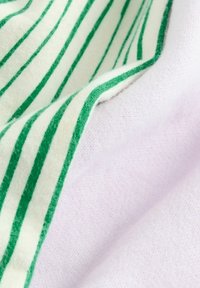 Bawełniana tkanina w zielono-białe poziome paski, charakteryzująca się miękką fakturą. Obok widoczny jest gładki biały fragment.