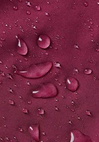 Gocce d'acqua di varie dimensioni su un tessuto liscio e profondo bordeaux, che evidenziano la trama resistente all'acqua e la lucentezza del tessuto.