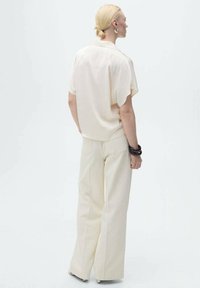 Cream short-sleeve blouse paired with light beige wide-leg trousers. Blouse features a relaxed fit. The overall look is minimalist and monochromatic.