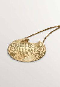 Colgante circular de oro con un patrón de olas texturizado, que presenta un detalle recortado. Cuelga de una cadena de metal trenzado.