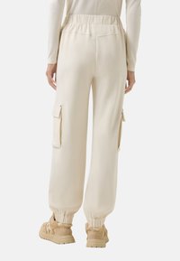 Beige cargobroek met een elastische tailleband, taps toelopende manchetten en twee zijzakken, gemaakt van een zachte stof met een gladde textuur.
