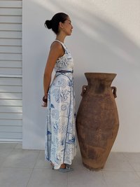 Rochie albă cu motive albastre, cu bust ajustat și fustă fluidă; alături de o vază mare din argilă brună, texturată, cu două forme.