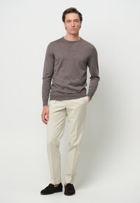 Maglione grigio a maniche lunghe, pantaloni crema e mocassini scuri. La vestibilità è rilassata con una texture liscia. Nessun motivo o accento visibile.