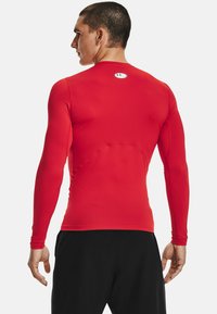 Rød langærmet sports Tshirt med en tætsiddende design, glat tekstur og et Under Armour-logo på bagsiden nær halsudskæringen.