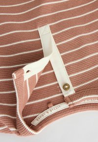 Randig topp i mjukt, ribbat material med en rosa och vit färgschema. Har en knappstängning och en etikett som visar märkesnamnet.