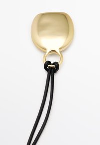 Ciondolo a forma di cucchiaio in metallo color oro con finitura liscia, attaccato a due cordini in pelle nera tramite un anello rotondo.