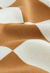 Braun-weiß gemusteter Stoff mit einer weichen, strukturierten Strickoptik und abwechselnden Rautenformen, die Wärme und Gemütlichkeit betonen.
