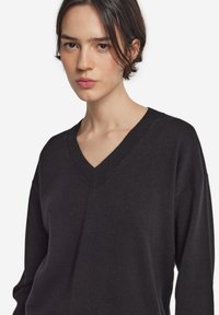 Czarny sweter w serek, wykonany z miękkiego materiału, o luźnym kroju i obniżonych ramionach, charakteryzujący się gładką fakturą i minimalnym zdobieniem.